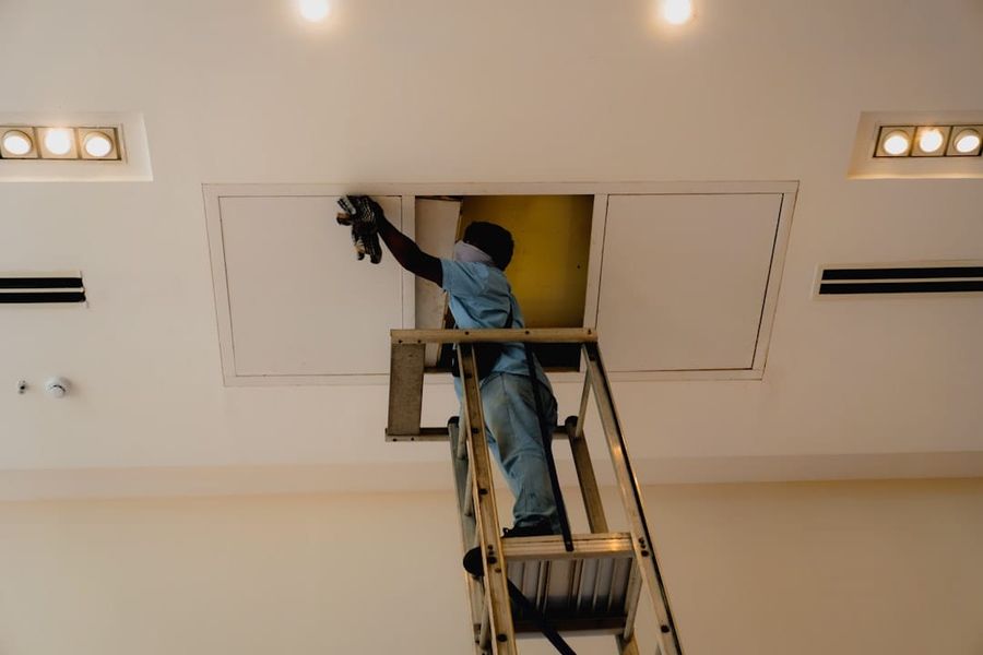 Certified technician performing air conditioning maintenance on a ceiling unit